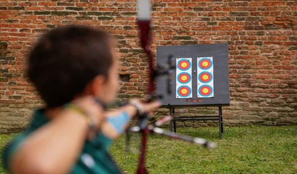 Ragazzo di spalle che lancia una freccia con l'arco verso il tiro a segno